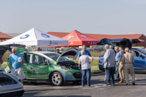 People stand around a green Chevy Bolt electric car with canopies in the background during JCREMC's EV Day event.